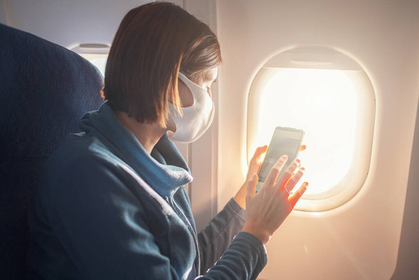 Young beautiful woman sitting at window of plane during the flight. new normal travel after covid-19 pandemic concept. taking photo from an airplane window - Photo, image