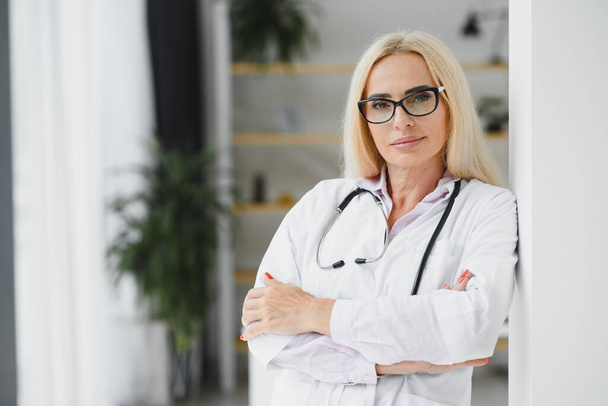Middle age woman wearing doctor uniform at clinic. - Фото, изображение
