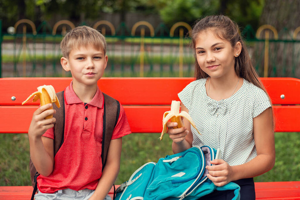 Los alumnos almorzan al aire libre sentados en el banco y comiendo frutas durante el descanso. - Foto, Imagen