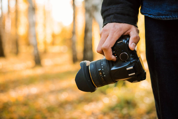 Tourist nature photographer holding camera in his hand shooting landscapes in autumn forest while golden sunset - Foto, afbeelding