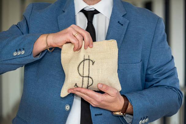 A middle-aged man in a business shirt holds a bag of dollars with an angry face. The concept of money you do not want to give - Fotografie, Obrázek