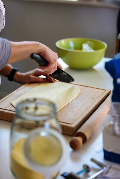 A vertical shot of a hand cutting a dough with a knife in the kitchen - Foto, imagen
