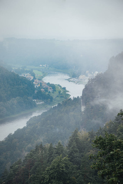 Photo looking down on the mountains at the Saxon Switzerland national park on a misty day with incredible rock formations shooting up from the ground - Фото, зображення