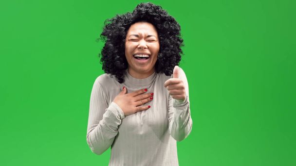 A beautiful shot of an African American young woman standing on a green chroma background and laughing hard - Valokuva, kuva