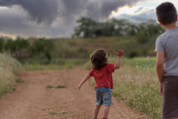 Two Caucasian boys walk through the field looking at a storm in the sky - Photo, Image