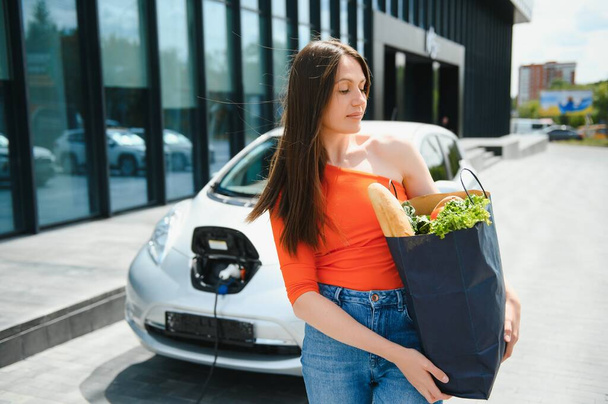 Eco electric car concept. Woman waiting electric car to charge - Foto, imagen