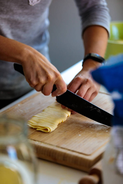 A vertical shot of a person cutting a dough with a knife in the kitchen - Foto, imagen