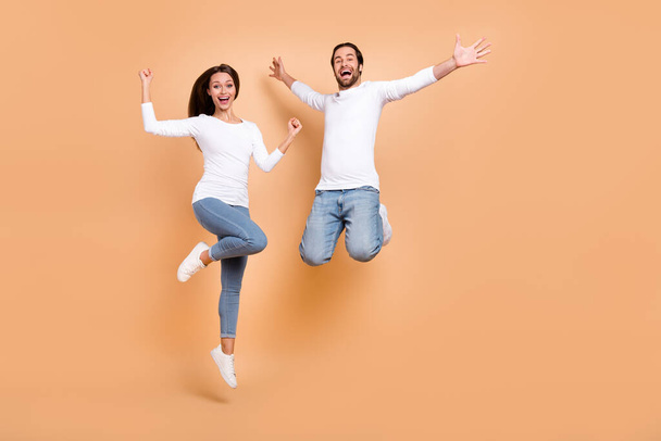 Full length body size view of two attractive cheery spouses jumping having fun isolated over beige pastel color background. - Foto, afbeelding
