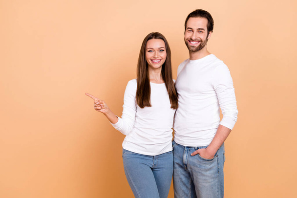 Photo of sweet young brunette couple index empty space wear white cloth isolated on beige color background. - Foto, afbeelding