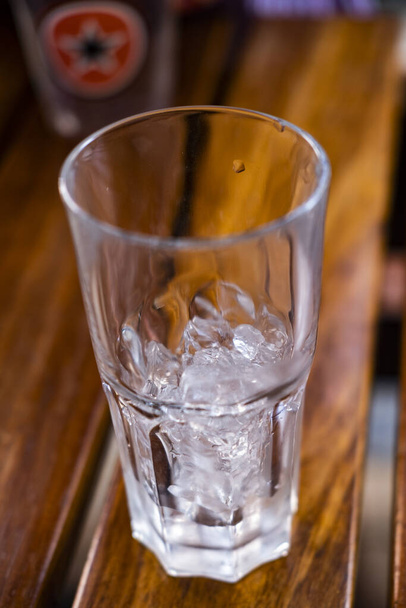 A függőleges közelkép egy átlátszó üveg kis jégkockák a fa polcon - Fotó, kép