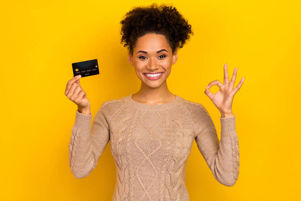 Fotografie ohromen Millennial brunetka dáma držet karty show okey nosit svetr izolované na žlutém pozadí. - Fotografie, Obrázek