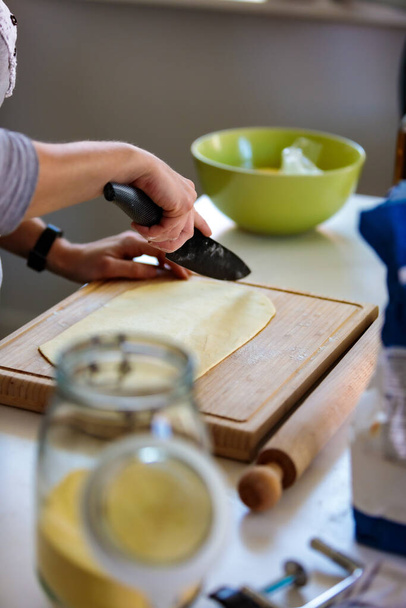 A vertical shot of a person cutting a dough with a knife in the kitchen - Zdjęcie, obraz