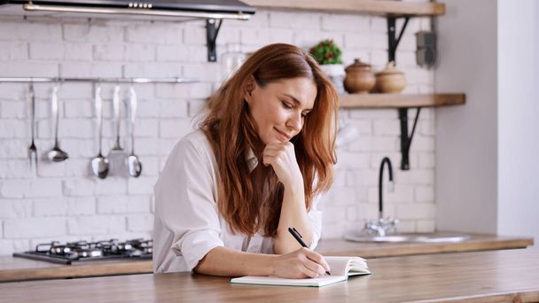 A Caucasian female writing something in her notebook in a kitchen - Foto, immagini