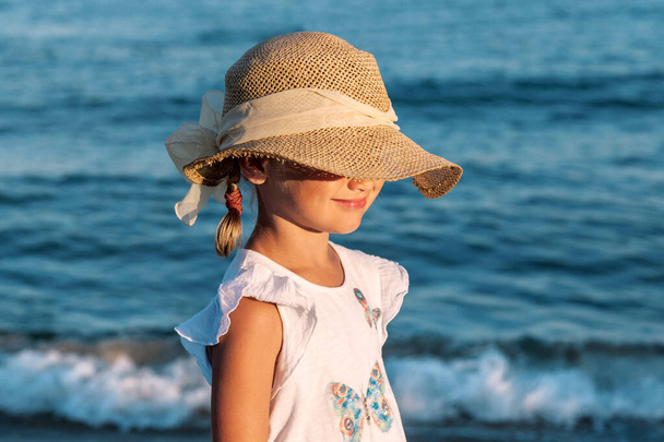 Sea Relax Summer holidays, vacation - beautiful little girl child wearing straw hat relaxing on beach near sea. Child in hat covering face from sun. Kid on sea lake background. - Foto, Bild