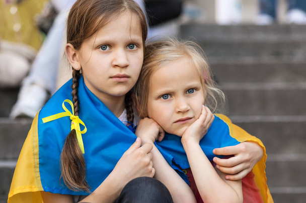 Ukrainian Children Refugee. Sad Migrant Children. Two frightened Girls wrapped in Ukraine Flag. Evacuation Kids from War Ukraine. - Fotó, kép