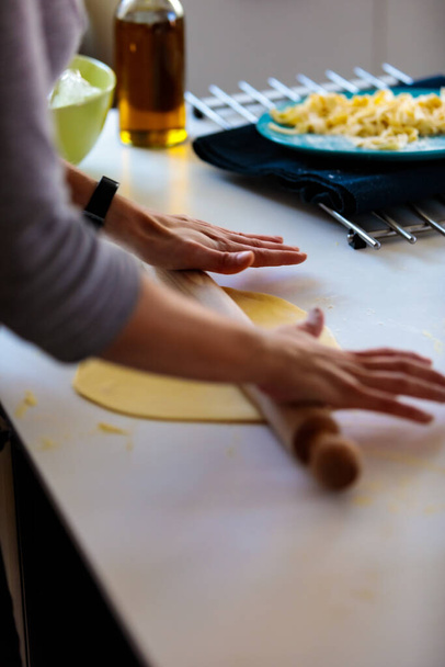 A vertical shot of a person rolling a dough with a rolling pin in the kitchen - Foto, imagen