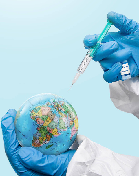A doctor injecting syringe of Coronavirus vaccine on the planet earth on a blue background - Φωτογραφία, εικόνα