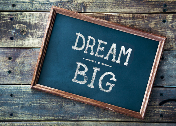 Hand drawn chalkboard sign DREAM BIG over old wooden table backg - Photo, Image
