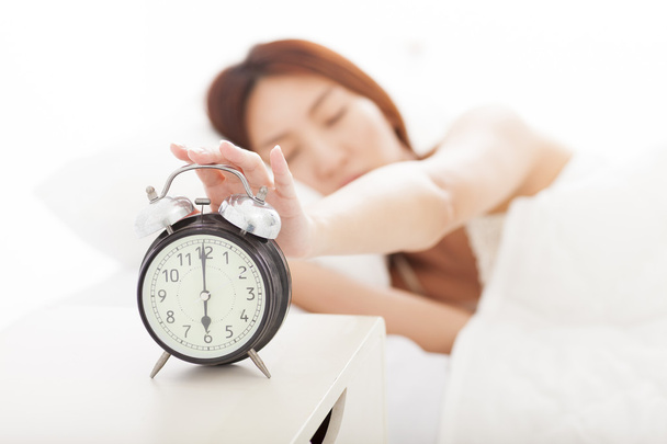 young Woman turning off the alarm clock on the bed - Photo, Image