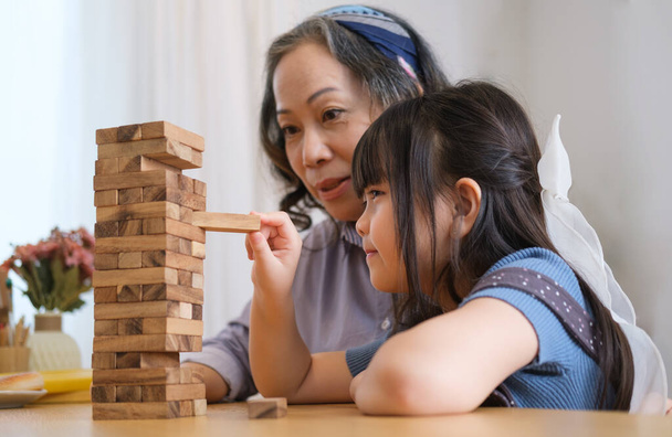 Küçük tatlı Asyalı kız, büyükannesiyle oturma odasında tahta bloklar oynuyor, hafta sonları birlikte mutlu vakit geçiriyor.. - Fotoğraf, Görsel