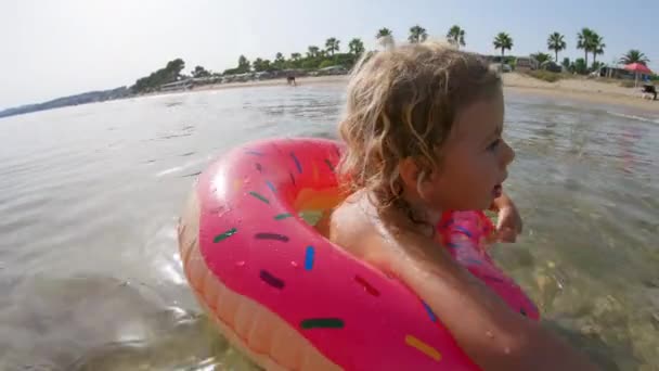 Mała dziewczynka pływająca i pływająca z nadmuchiwanym pierścieniem w morzu - Materiał filmowy, wideo