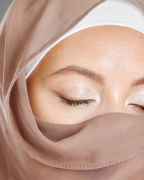 Mujer árabe modesta que usa maquillaje con la cara cubierta de un hiyab tradicional marrón. Primer plano de una hermosa joven musulmana con la piel radiante y los ojos cerrados con un pañuelo religioso que cubre. - Foto, Imagen