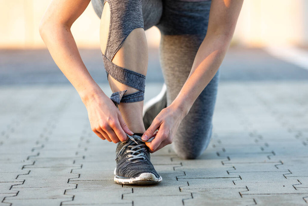 A closeup of a young woman doing fitness and ties shoelaces in nature - Photo, Image