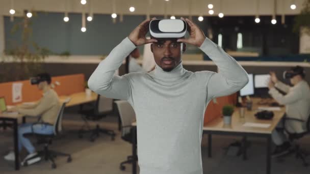 Pracownik biurowy ubrany w słuchawki VR, koncepcja rzeczywistości wirtualnej. Portret afrykańskiego dewelopera oprogramowania stojącego w biurze. To, biznes i koncepcja nowych technologii - Materiał filmowy, wideo