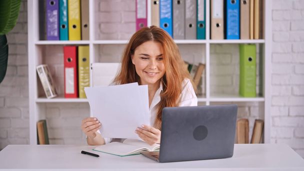 A Caucasian female reading documents in front of a laptop - Fotó, kép