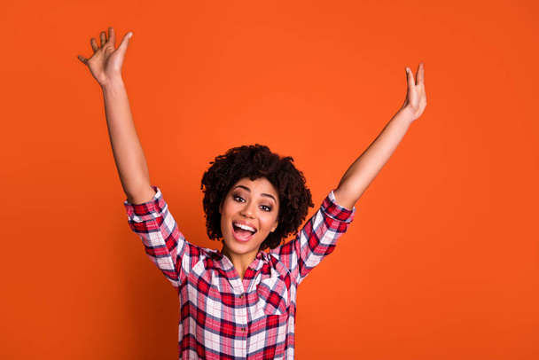 Photo of adorable excited lady dressed checkered shirt rising arms smiling isolated orange color background. - Photo, image