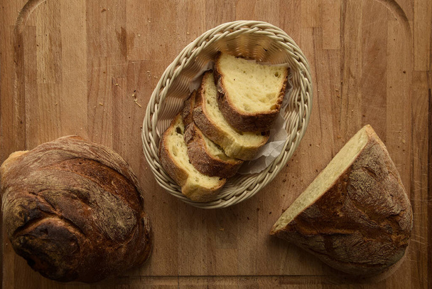 A freshly baked bread sliced in a wicker basket on a wooden table in the kitchen - Foto, Imagem