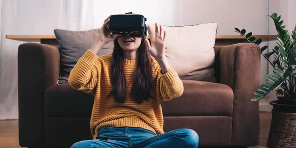 Ασιάτισσα γυναίκα παίζουν VR παιχνίδι για διασκέδαση στο σπίτι, Ασιάτισσα γυναίκα χαρούμενη στο σπίτι για διακοπές. Ευτυχισμένη γυναίκα που παίζει την έννοια της τεχνολογίας metaverse VR - Φωτογραφία, εικόνα
