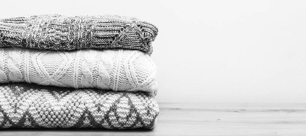 Pile of sweaters on table. Autumn, winter season knitwear. Knitted color clothes, vintage style. Clean woolen clothes in stack. Stack of knitted warm clothes on wooden background. - Photo, Image