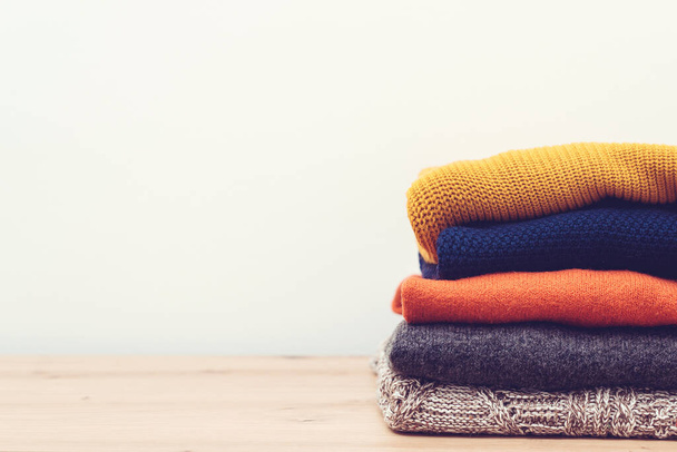 Clean woolen clothes in stack. Stack of knitted warm clothes on wooden background. Pile of sweaters on table. Autumn, winter season knitwear. Knitted color clothes, vintage style. - Photo, Image