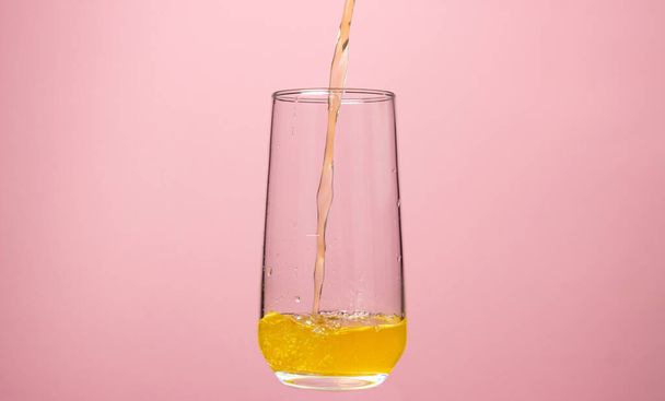 Glass of juice on a pink background. Orange juice is poured into a glass. Delicious and refreshing drink - Zdjęcie, obraz