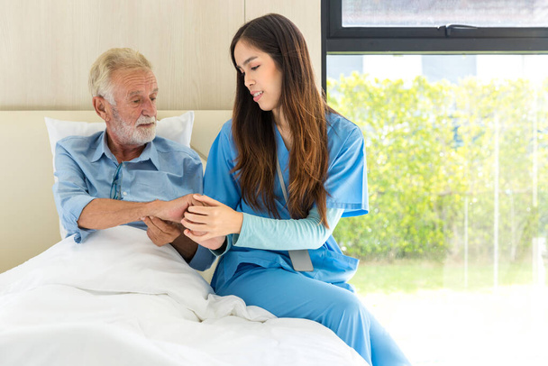 Медсестра, использующая монитор артериального давления для пожилых пациентов, сидит на кровати. Медсестра помогает пожилому человеку - Фото, изображение