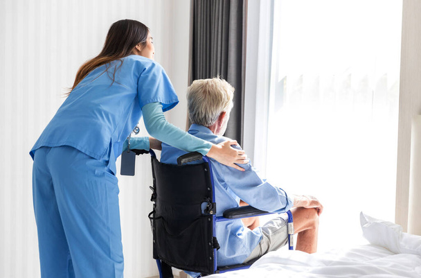 Η νοσοκόμα φροντίζει έναν ηλικιωμένο ασθενή που κάθεται σε αναπηρικό καροτσάκι. Νοσοκόμα βοηθά πρεσβύτερους - Φωτογραφία, εικόνα