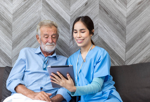 Nurse helping patient for using tablet. Caretaker and senior man using tablet PC at nursing home - Foto, Imagen