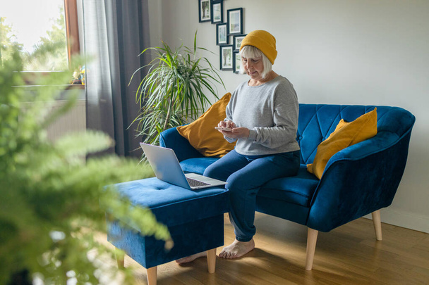Концентрована зріла красива блондинка 50-х років використовує ноутбук на дивані вдома
 - Фото, зображення