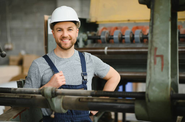 Smiling and happy employee. Industrial worker indoors in factory. Young technician with white hard hat - Φωτογραφία, εικόνα