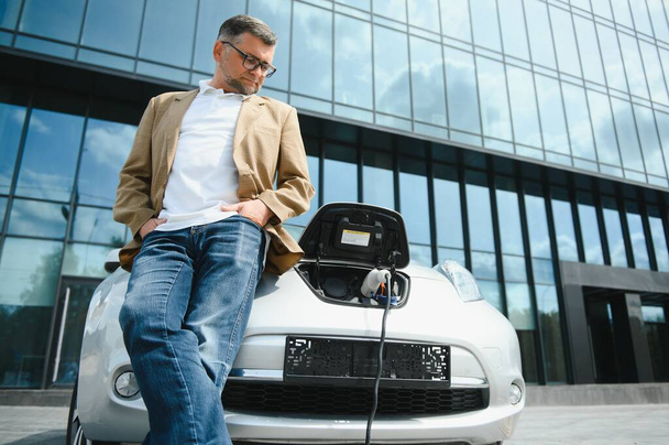 Man charges an electric car at the charging station. - 写真・画像
