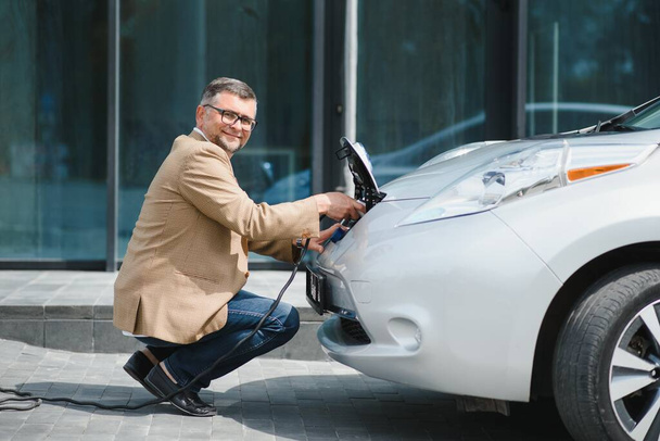 a businessman charges an electric car. - Foto, Imagem