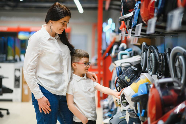 Mother and son shopping for electric vacuum cleaner, smiling. - Foto, afbeelding