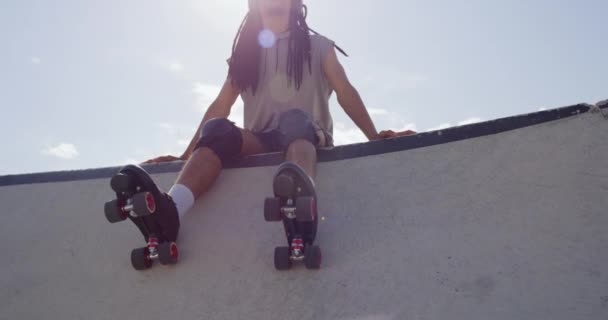 Ein Mann mit langen Dreadlocks und Rollerblades amüsiert sich in einem Skatepark. Skater-Junge entspannt sich mit Kopfhörern und hört draußen Musik. Cooler Typ, der Zeit im Freien verbringt. - Filmmaterial, Video