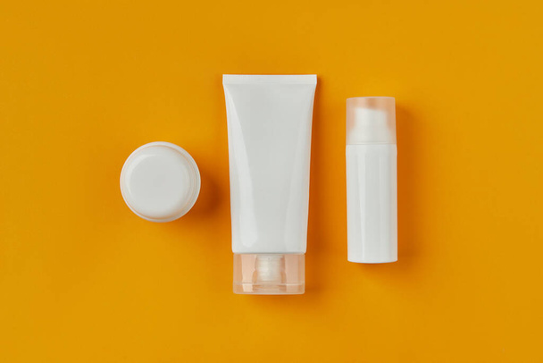 Flat lay top view blank white tubes bottles with skin care products on orange creative background. Facial body treatment wellness concept. - Photo, Image