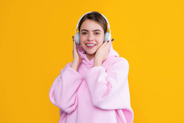 усміхнена дівчина слухає музику в навушниках на жовтому фоні
. - Фото, зображення