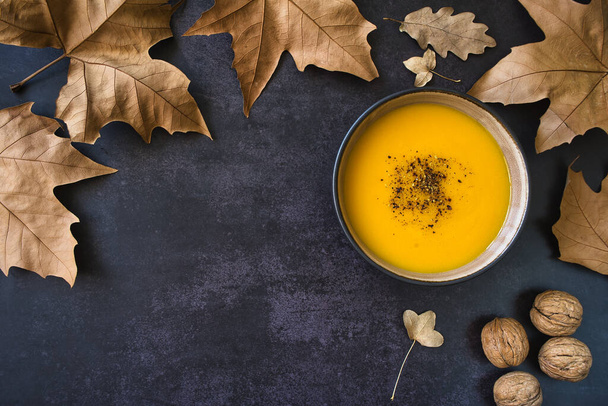 Autumnal composition with dried leaves and delicious creamy homemade vegetables soup on dark background. Copy space - Fotó, kép