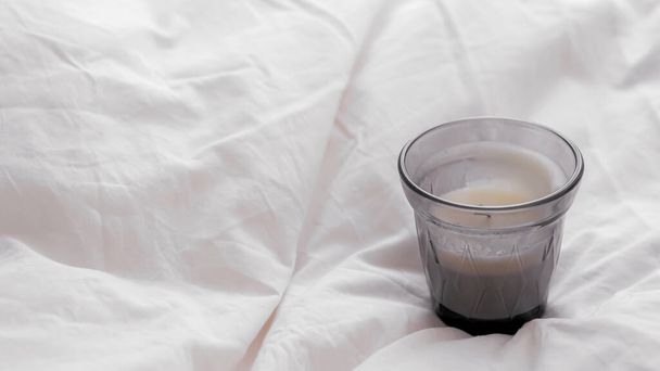 A closeup shot of a small candle glass cup with on a white bed sheet - Fotoğraf, Görsel