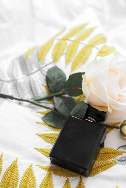 A vertical shot of a luxury perfume bottle on a pillow with a rose - Fotó, kép
