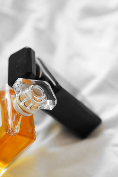 A vertical shot of two perfume bottles on a white bedsheet on a blurred background - Zdjęcie, obraz